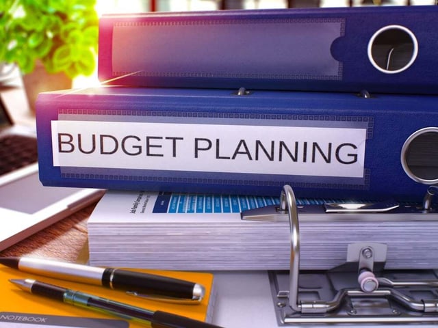 Blue Ring Binder with Inscription Budget Planning on Background of Working Table with Office Supplies and Laptop. Budget Planning Business Concept on Blurred Background. 3D Render..jpeg